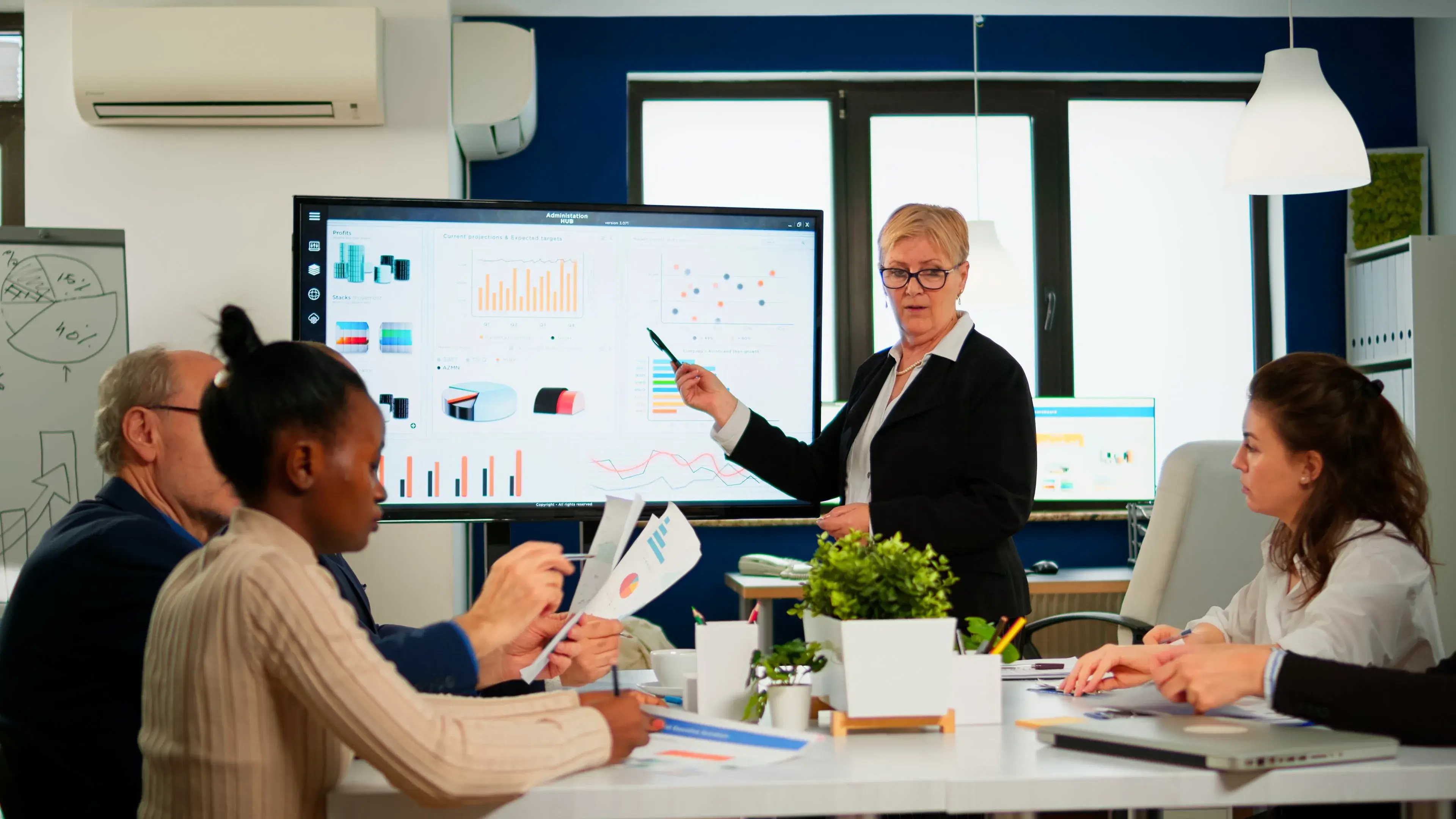 A manager presenting charts on a large screen to her team