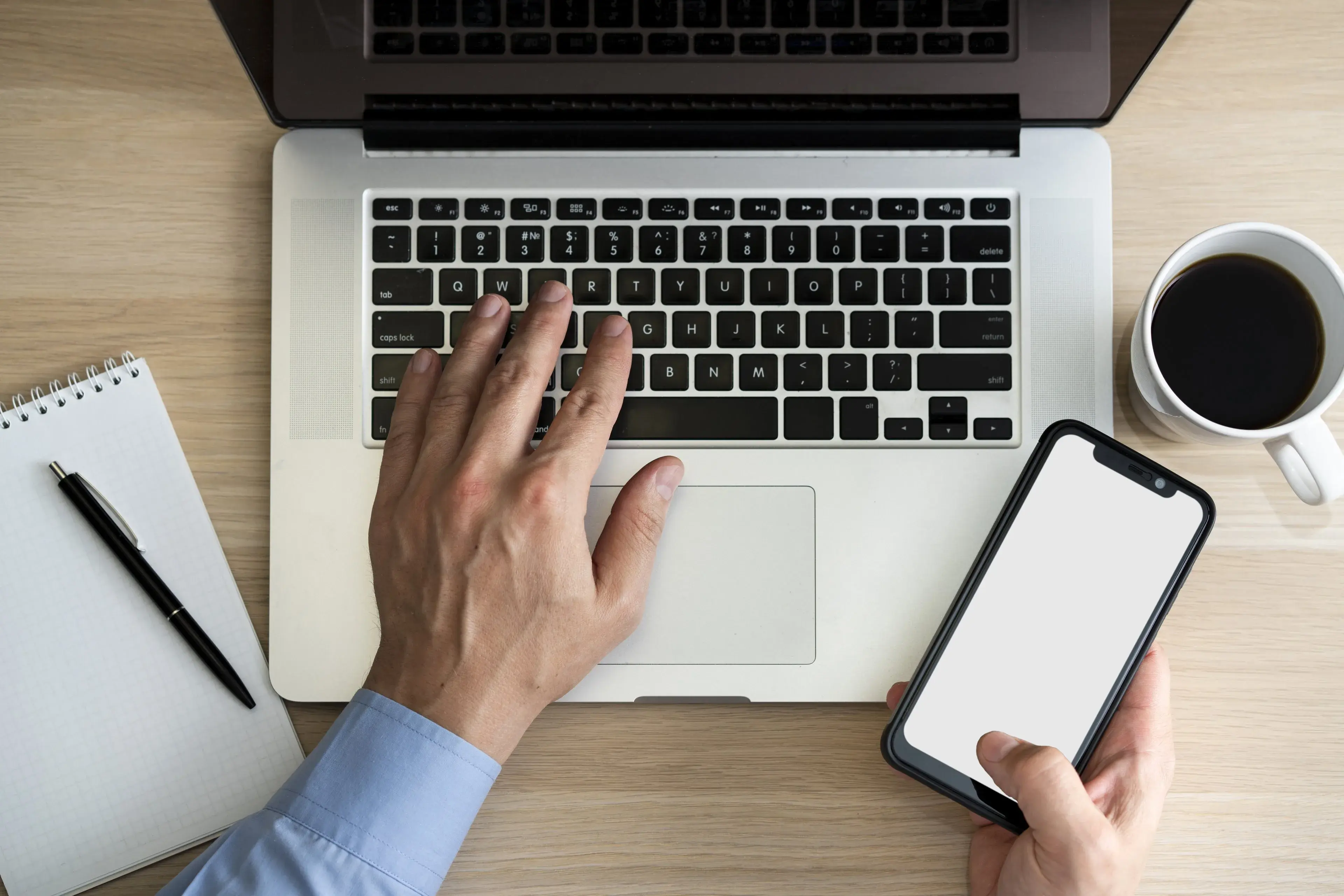 Hands working on a laptop while holding a smartphone