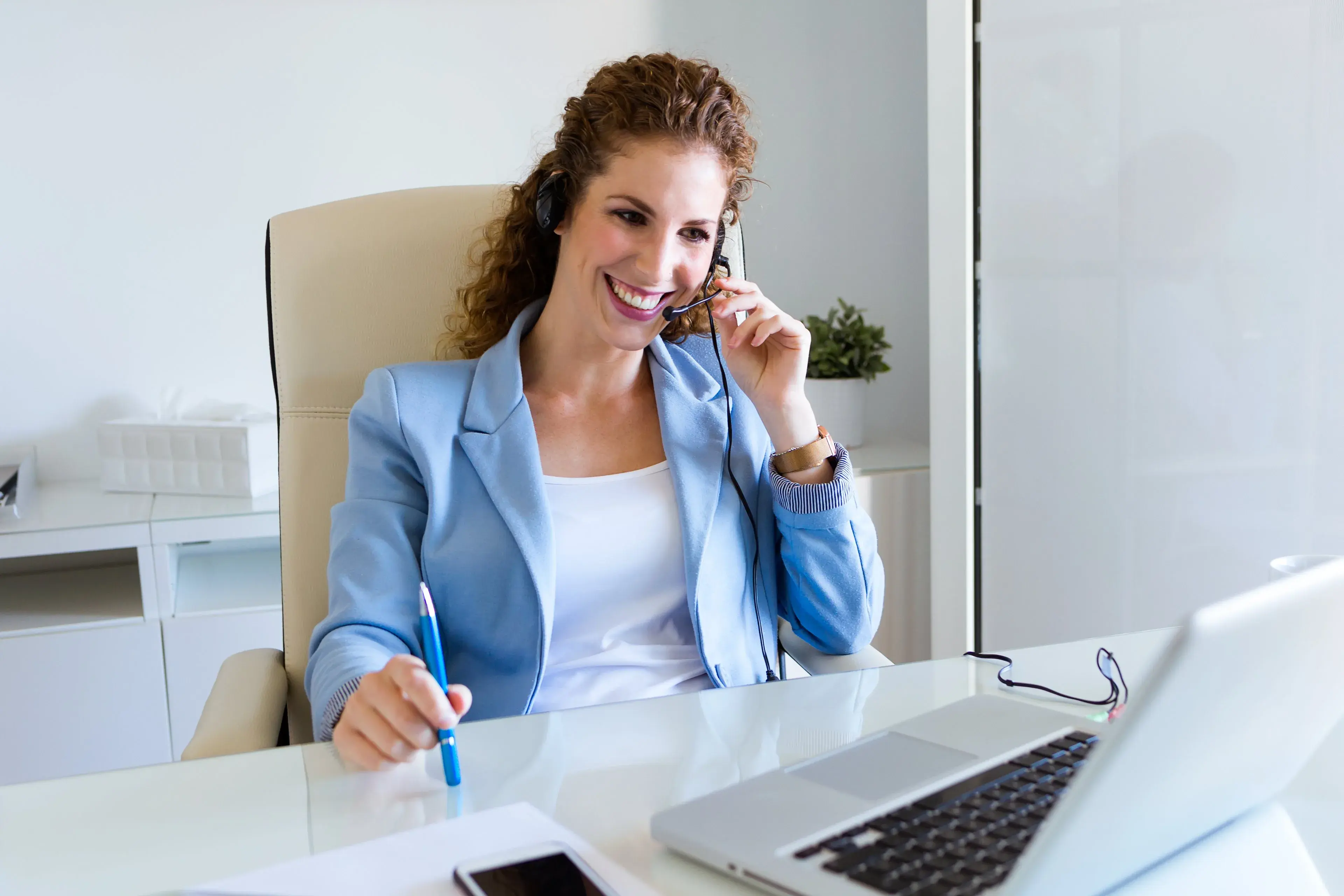 A professional smiling while taking a phone call at her desk
