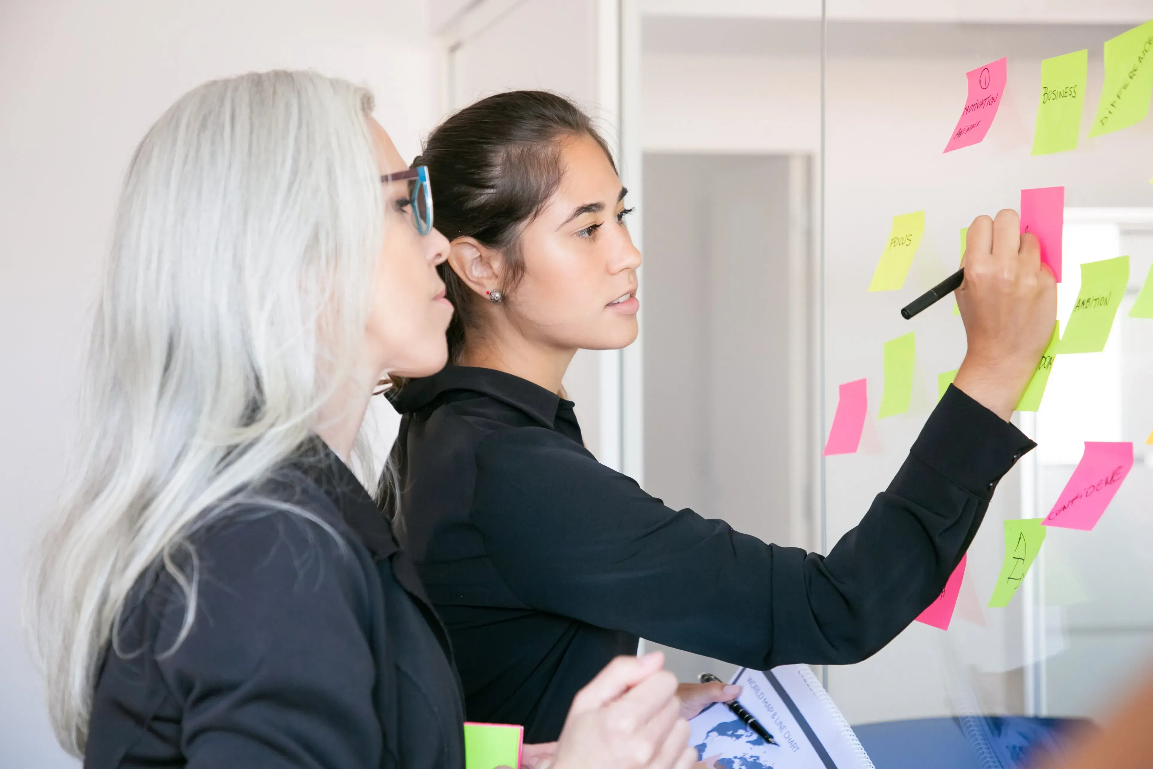 Two colleagues mapping a process with sticky notes on a glass wall