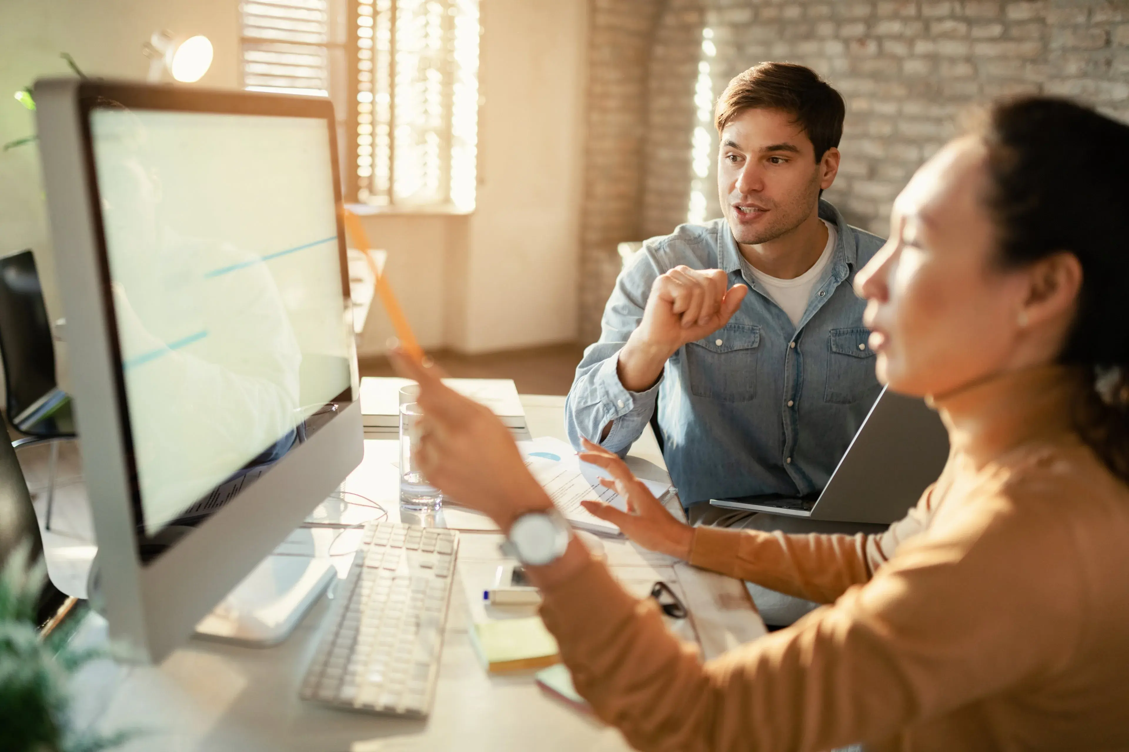 Two colleagues discussing work on a desktop computer