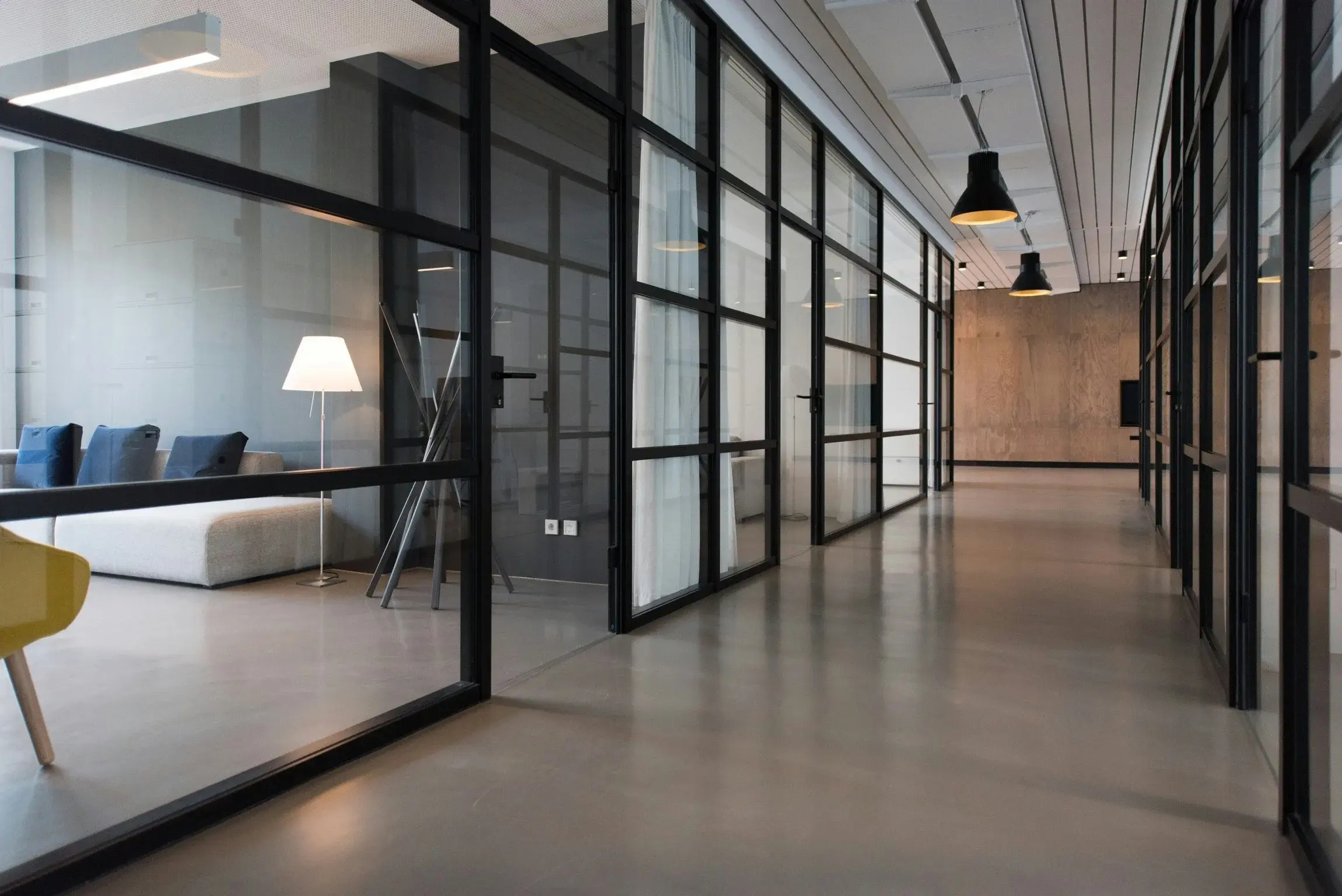 A bright office corridor lined with glass-walled meeting rooms