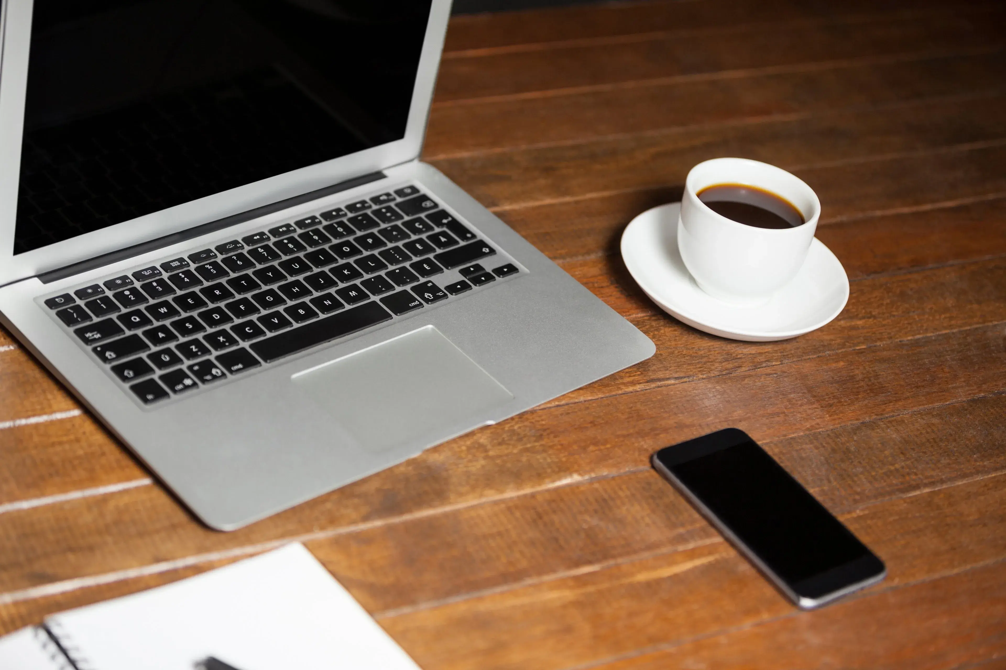A laptop, phone and coffee on a timber desk