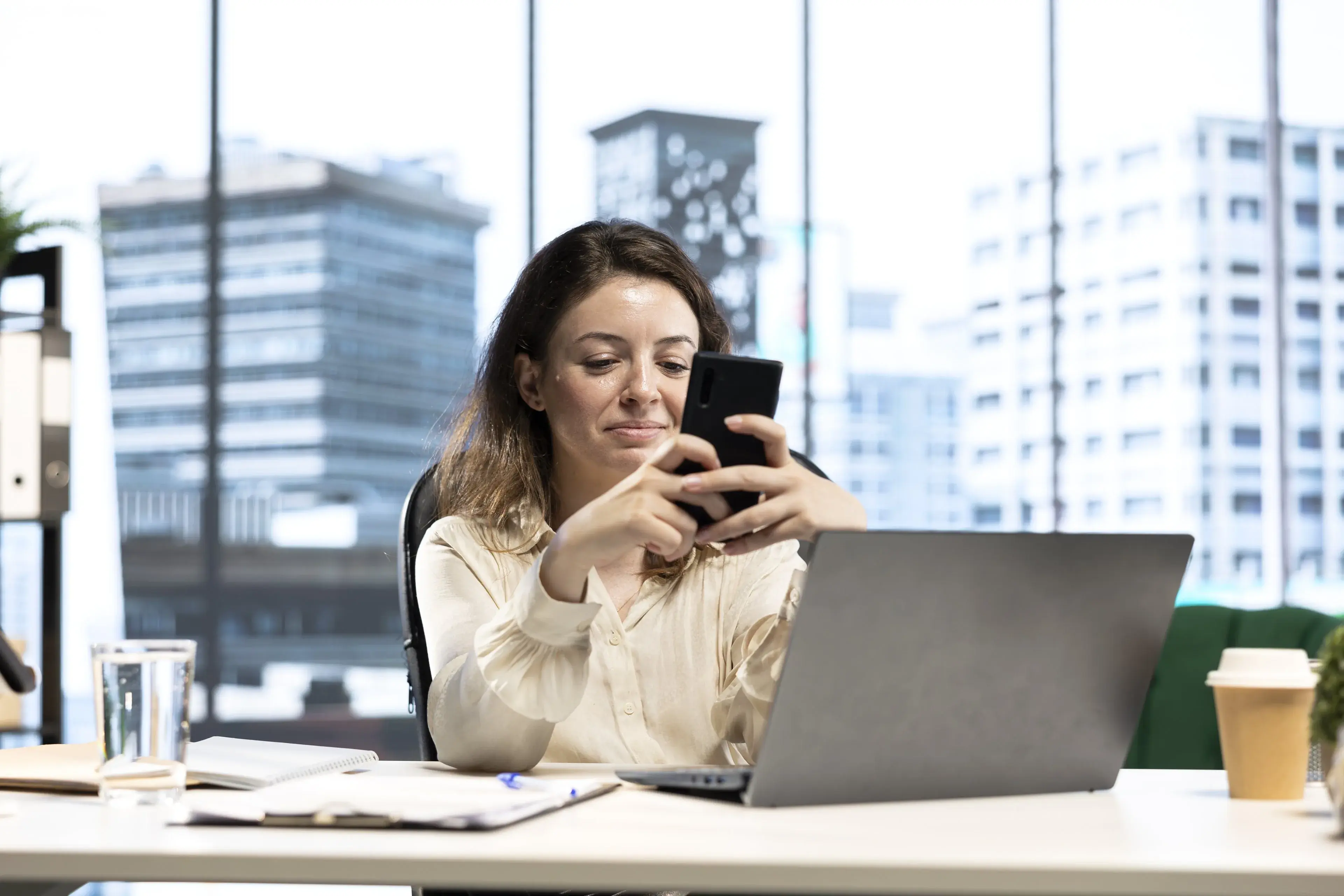 A professional reading a message on her phone at her desk